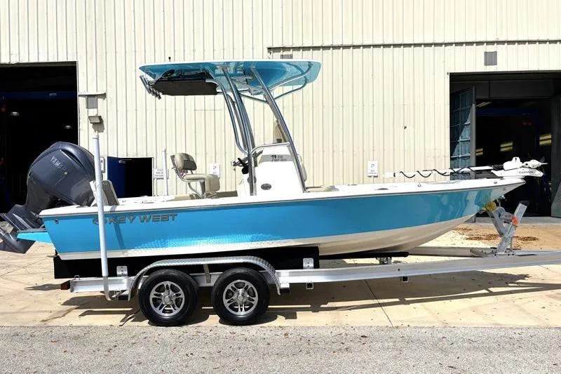The Image of 2025 Key West 210 Bay Reef boat on trailer, blue hull, parked outside a building. - 0