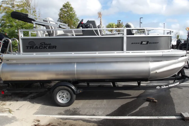 The Image of 2026 Sun Tracker Bass Buggy 16 XL Select pontoon boat on trailer, parked outdoors. - 1