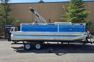 The Image of 2026 Sun Tracker Fishin' Barge 20 DLX pontoon boat on trailer, parked outdoors. - 0