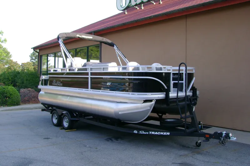 Slide: The Image of 2026 Sun Tracker Fishin' Barge 20 DLX pontoon boat on trailer, parked outdoors. - 1
