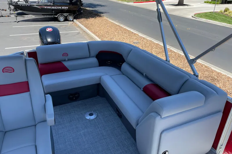 Slide: The Image of 2026 Sun Tracker Party Barge 20 DLX interior with gray and red seating, parked outdoors. - 9
