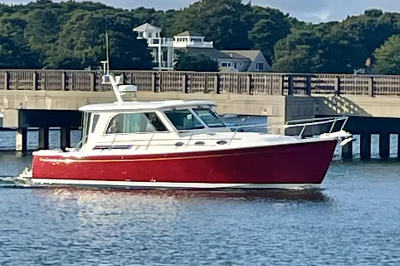 Slide: The Image of 2011 Back Cove 37 boat with red hull cruising near a bridge. - 1