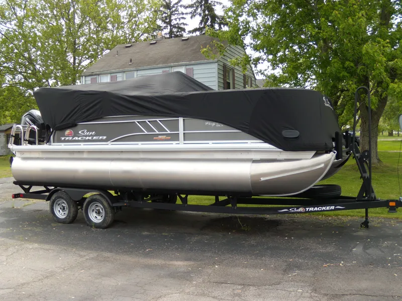 The Image of 2023 Sun Tracker Party Barge 20 DLX pontoon boat on trailer, covered, parked outdoors. - 0