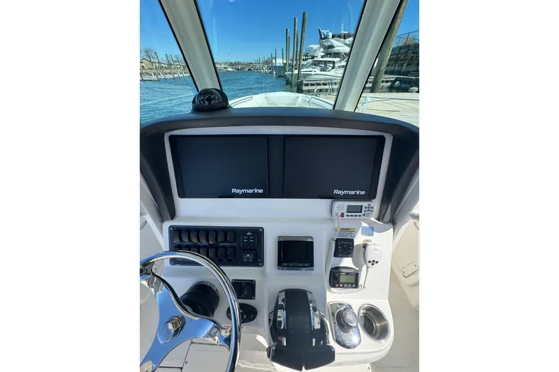 Slide: The Image of 2014 Boston Whaler 280 Outrage helm with Raymarine displays and controls, docked by the water. - 6
