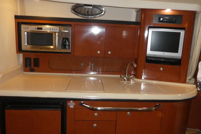 Slide: The Image of 2005 Sea Ray 340 Sundancer galley with microwave, sink, and TV in wooden cabinetry. - 13