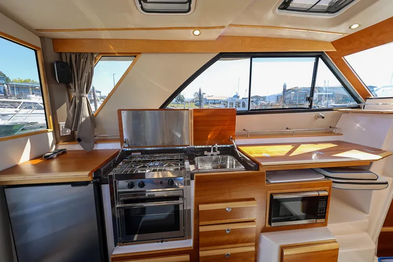Slide: The Image of 2019 Cutwater C-302 Coupe interior kitchen with stove, sink, and wooden cabinetry. - 20