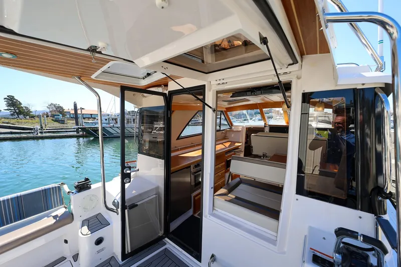 Slide: The Image of 2019 Cutwater C-302 Coupe interior view with open doors, showcasing seating and marina backdrop. - 5