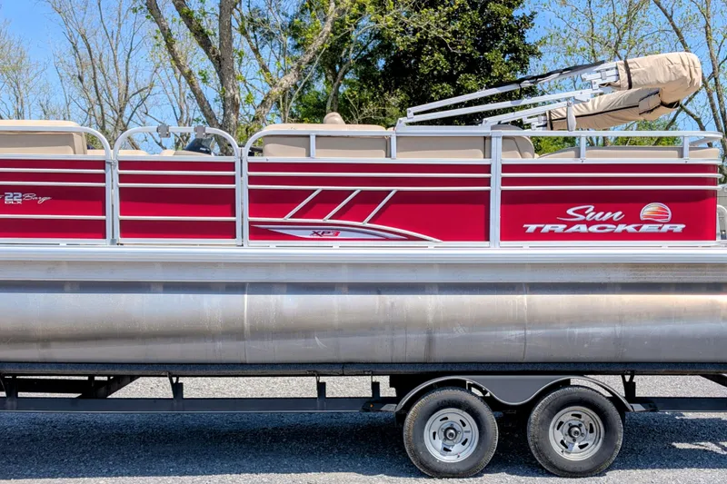 The Image of 2020 Sun Tracker pontoon boat with red exterior on a trailer, surrounded by trees. - 0
