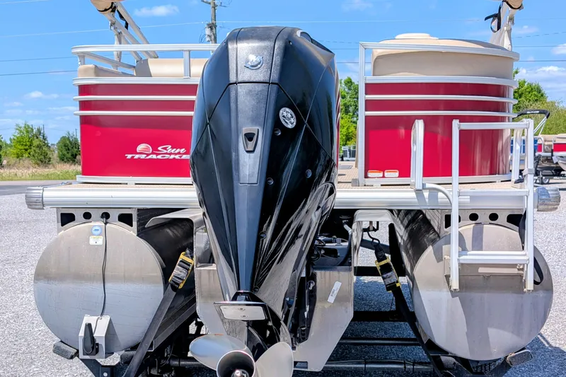 Slide: The Image of 2020 Sun Tracker pontoon boat with outboard motor, red and white design, parked outdoors. - 2