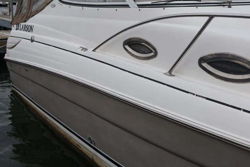 Slide: The Image of 2006 Larson Cabrio 240 boat docked, showcasing sleek design and porthole windows. - 52