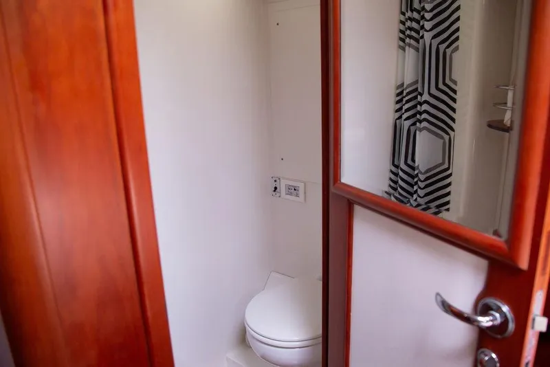 Slide: The Image of Compact bathroom with wooden door on 2015 Outbound 46 yacht, featuring modern fixtures and geometric shower curtain. - 54