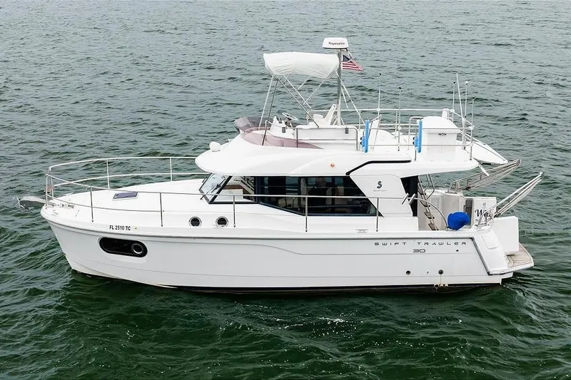 Slide: The Image of 2018 Beneteau Swift Trawler 30 cruising on open water near a scenic shoreline. - 18