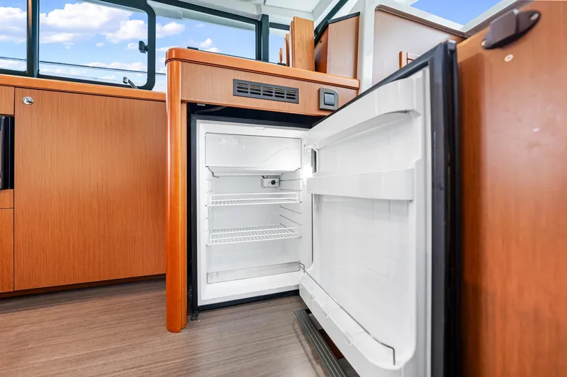 Slide: The Image of Open refrigerator inside 2018 Beneteau Swift Trawler 30, showcasing modern wooden interior design. - 50