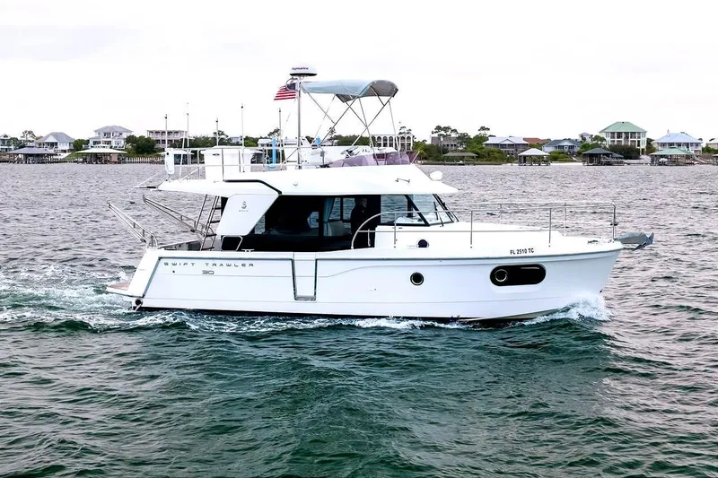 Slide: The Image of 2018 Beneteau Swift Trawler 30 cruising on open water near coastal homes. - 6