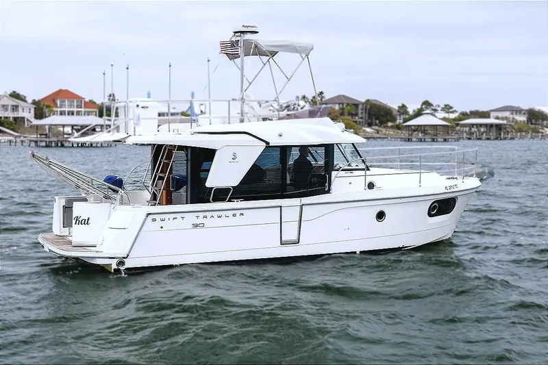 Slide: The Image of 2018 Beneteau Swift Trawler 30 cruising on water near coastal homes. - 7
