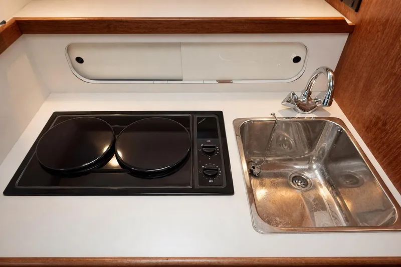 Slide: The Image of Compact kitchen area in a 1997 Tiara 3100 Open Express boat, featuring a stove and sink. - 21
