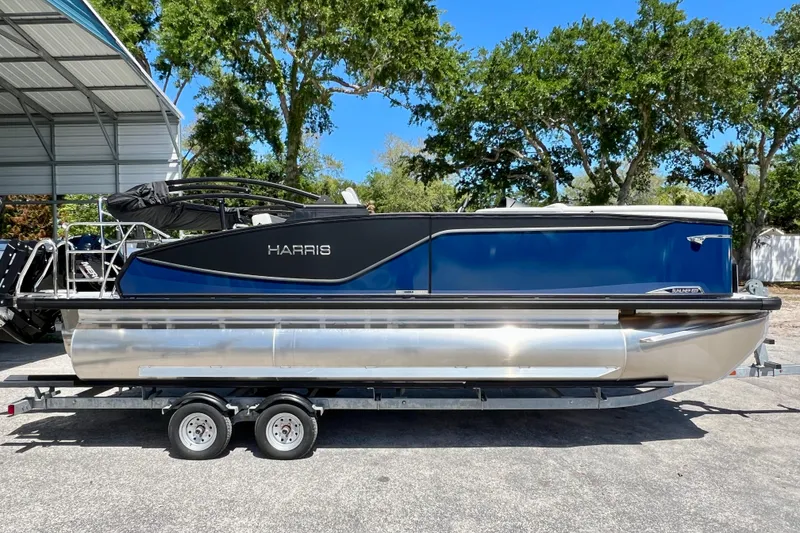 The Image of 2026 Harris Sunliner 210 pontoon boat on trailer, parked outdoors under a canopy. - 1