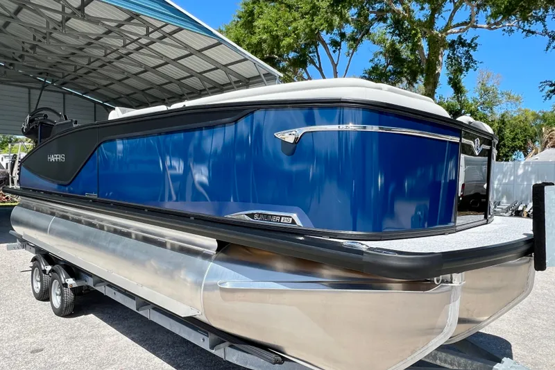 Slide: The Image of 2026 Harris Sunliner 210 pontoon boat with sleek blue design on a trailer. - 2
