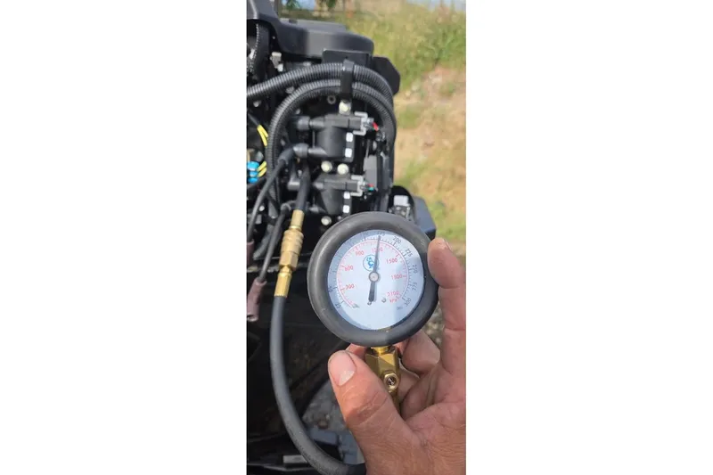 Slide: The Image of Hand holding pressure gauge near Tracker Pro Guide V-16 SC engine, 2021 model. - 48