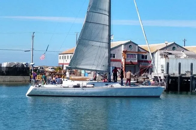 The Image of 1986 Bill Lee Yachts Santa Cruz 50 sailboat docked near rustic waterfront buildings. - 1