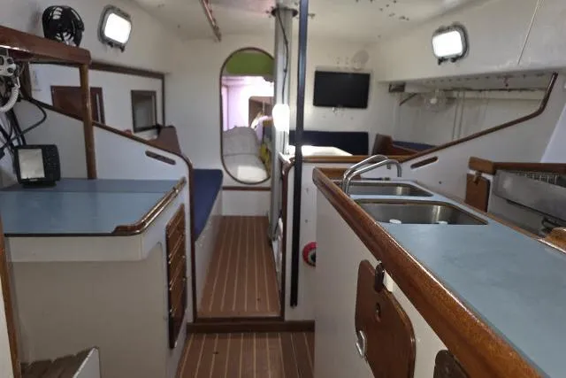 Slide: The Image of Interior of 1986 Bill Lee Yachts Santa Cruz 50, featuring a compact kitchen and seating area. - 4