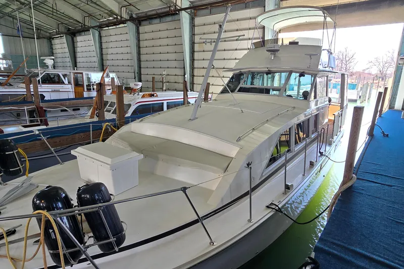 The Image of 1977 Bertram 42 Flybridge Motor Yacht docked in a marina, sheltered under a large structure. - 0