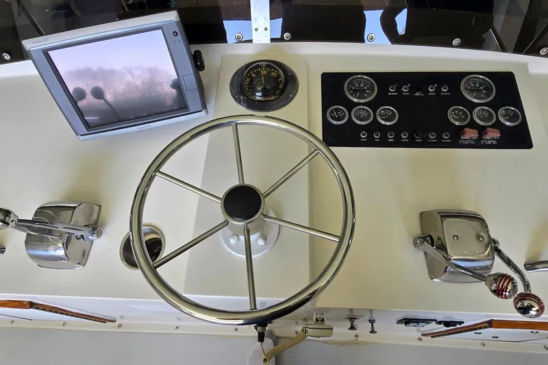 Slide: The Image of 1977 Bertram 42 Flybridge Motor Yacht helm with steering wheel, gauges, and navigation screen. - 16