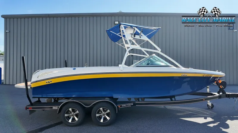 The Image of 2005 Nautique SV-211 boat on trailer in front of gray building. - 1