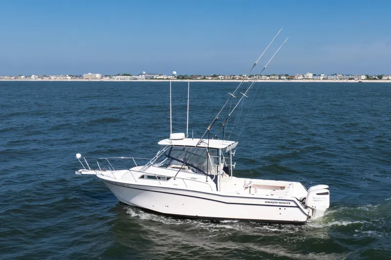 Slide: The Image of 1997 Grady-White Marlin 300 boat cruising on open water near a coastal town. - 28