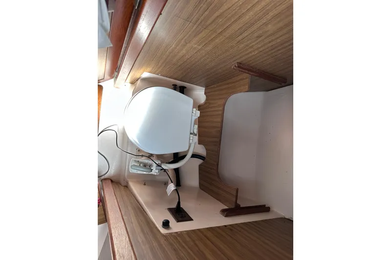 Slide: The Image of 1975 Cape Dory 28 interior showing a compact marine toilet setup with wooden paneling. - 17