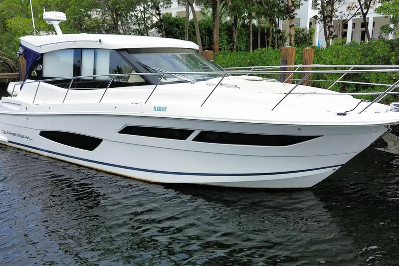 Slide: The Image of 2021 Regal 38 XO yacht docked on calm water, surrounded by lush greenery. - 11