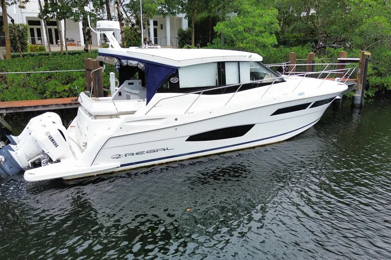 Slide: The Image of 2021 Regal 38 XO yacht docked by lush greenery and waterfront homes. - 14