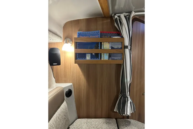 Slide: The Image of 2024 Ranger Tugs R-27 interior with wooden shelf, books, and striped curtain. - 13