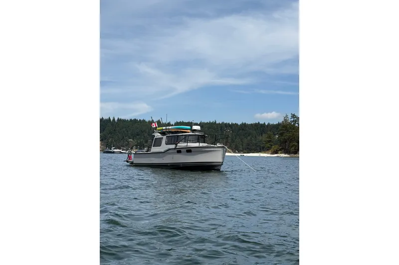 Slide: The Image of 2024 Ranger Tugs R-27 boat anchored on scenic water with forested shoreline. - 2