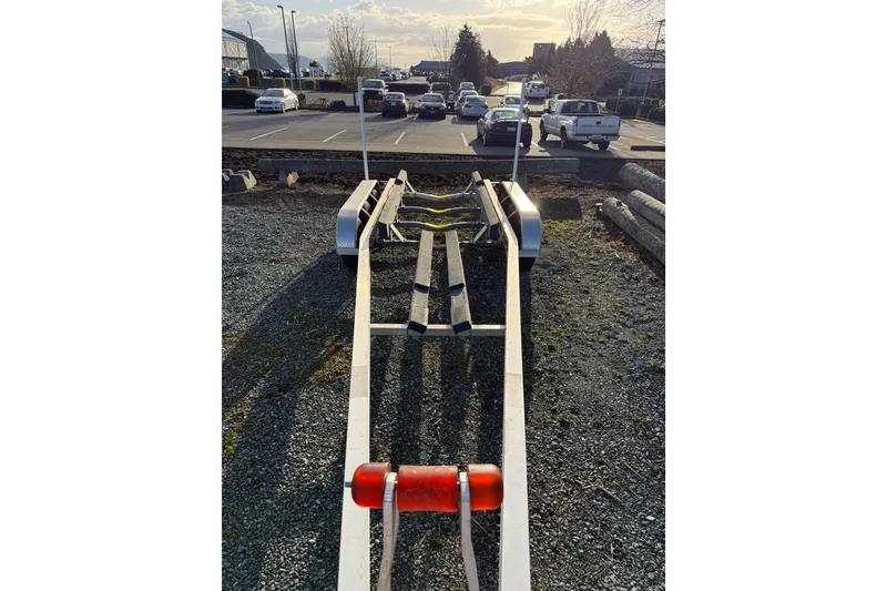 Slide: The Image of Boat trailer for 2024 Ranger Tugs R-27 on gravel, with parked cars in background. - 23