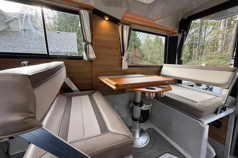 Slide: The Image of 2024 Ranger Tugs R-27 interior with seating and wooden table, surrounded by windows. - 9