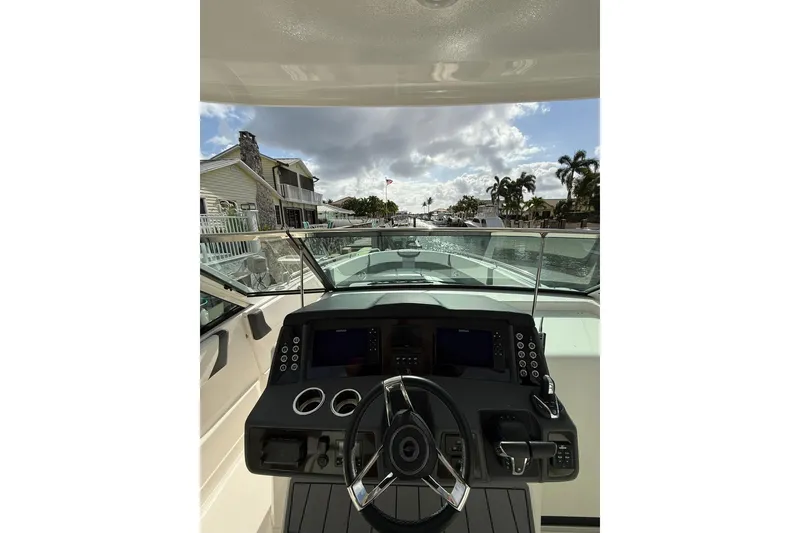 Slide: The Image of 2023 Chaparral 300 OSX boat dashboard with steering wheel, dockside view, and clear sky. - 37
