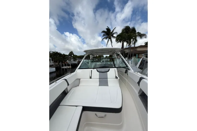 Slide: The Image of 2023 Chaparral 300 OSX boat interior with white seating, palm trees, and cloudy sky. - 44