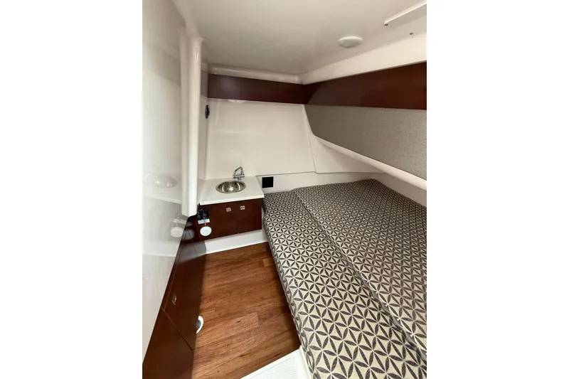 Slide: The Image of 2023 Chaparral 300 OSX cabin interior with patterned bedding and compact sink area. - 54