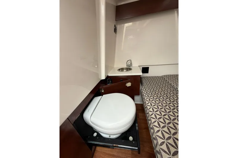 Slide: The Image of 2023 Chaparral 300 OSX cabin interior with toilet, sink, and patterned bedding. - 58