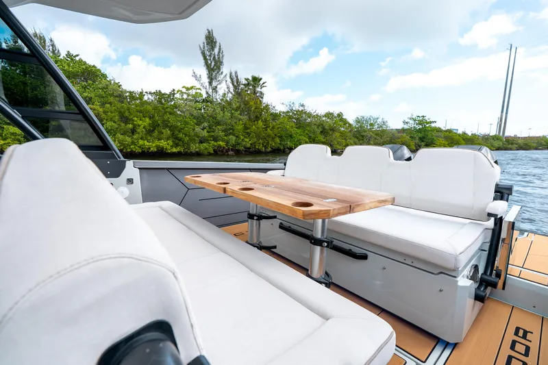 Slide: The Image of 2024 Saxdor 320 GTO boat interior with white seating and wooden table, near lush greenery. - 11
