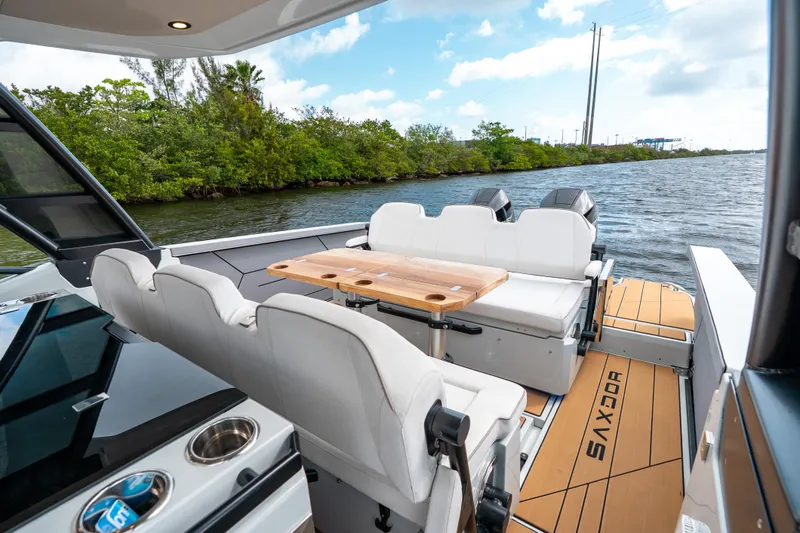 Slide: The Image of 2024 Saxdor 320 GTO boat interior with seating and table on a scenic waterway. - 12