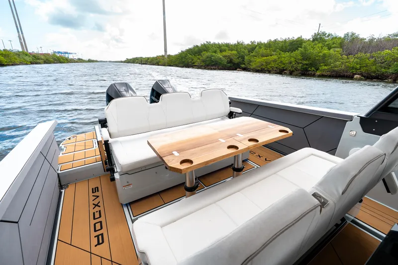 Slide: The Image of 2024 Saxdor 320 GTO boat interior with seating and table on a scenic waterway. - 14