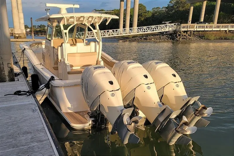 The Image of 2018 Scout 355 LXF boat docked with triple outboard engines in a scenic marina. - 0