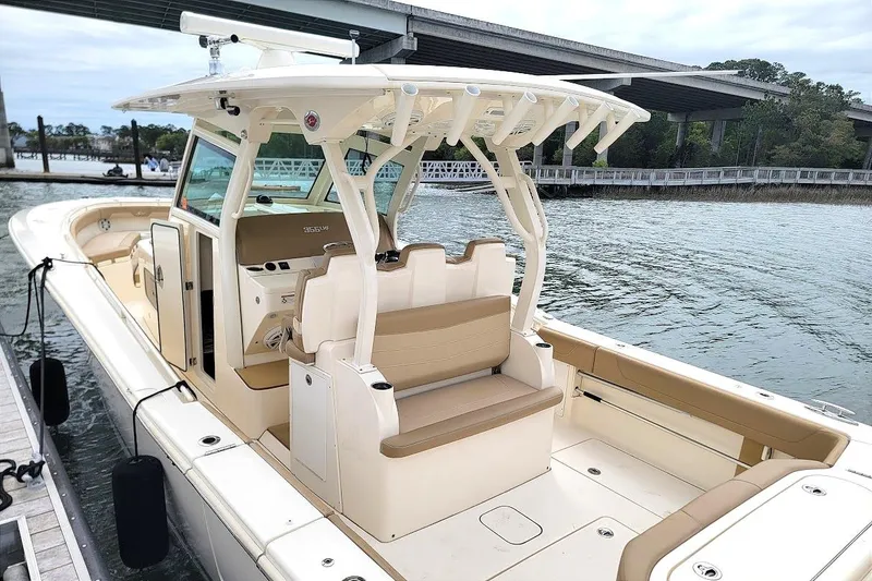 Slide: The Image of 2018 Scout 355 LXF boat docked by a bridge, featuring spacious seating and modern design. - 14