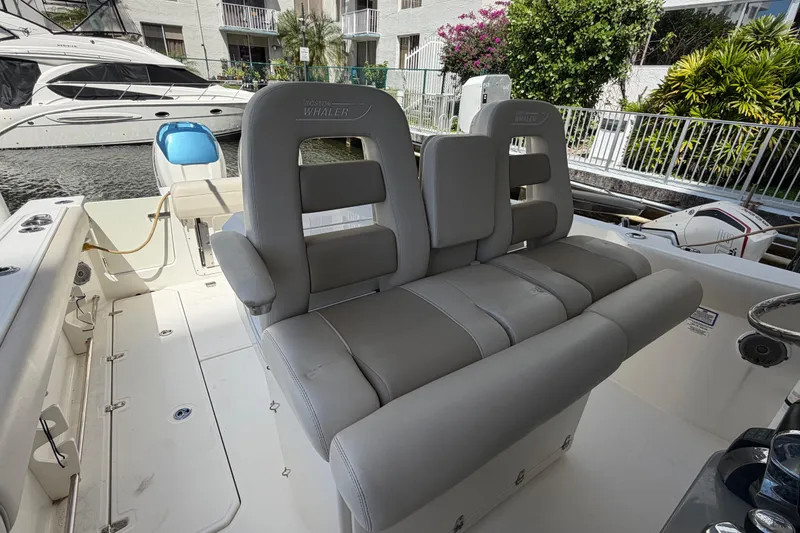 Slide: The Image of 2016 Boston Whaler 330 Outrage boat interior with gray seating and marina backdrop. - 17