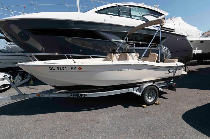 The Image of 2023 Scout 175 Sportfish boat on trailer, parked beside larger yachts. - 1