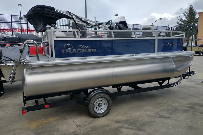 The Image of 2026 Sun Tracker Bass Buggy 16 XL Select pontoon boat on trailer, parked outdoors. - 0
