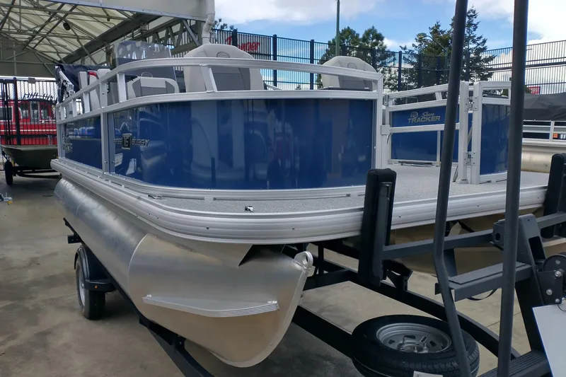 Slide: The Image of 2026 Sun Tracker Bass Buggy 16 XL Select pontoon boat on trailer, displayed outdoors. - 2