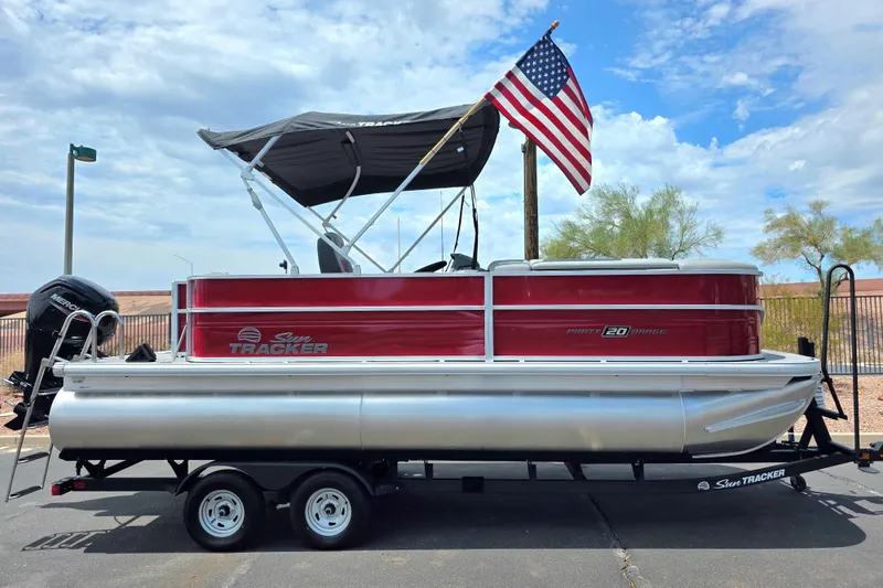 The Image of 2026 Sun Tracker Party Barge 20 DLX pontoon boat with American flag on trailer. - 0